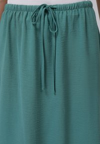 Teal, struktureret nederdel med elastisk talje og snøre. Mellemlangt design med et blødt, krøllet stof.