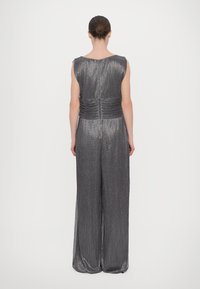Jumpsuit argento plissettato con gambe ampie, design senza maniche e dettaglio arricciato sulla schiena. Texture liscia e lucentezza metallica.