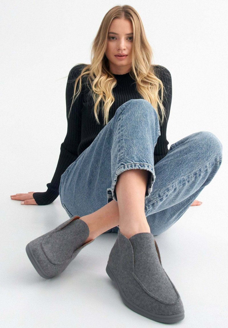 Szare, wsuwane buty na niskim obcasie o zaokrąglonym kształcie. Posiadają brązowy akcent na pięcie oraz teksturowaną powierzchnię. Ocasualnym stylu.