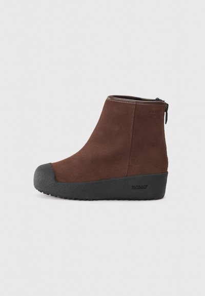 Braune Wildleder-Stiefelette mit runder Spitze, strukturiertem schwarzem Gummisohle und seitlichem Reißverschluss. Dezente Markierung an der Ferse und in der Nähe des Reißverschlusses.