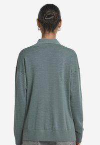 Långärmad grön tröja med ribbad krage och muddar, med en avslappnad passform och mjuk textur. Baksidan har en diskret, slät yta.