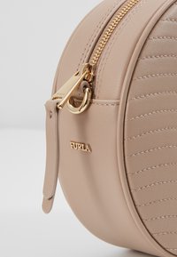 Runde beige Lederhandtasche mit gesteppter Struktur, ausgestattet mit einem goldenen Reißverschluss und Beschlägen, geprägtem Logo und einem kleinen Tragriemen.