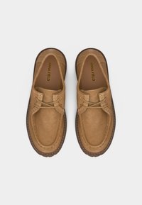 Paire de chaussures style mocassin en daim beige avec détails de coutures et lacets, vue de dessus sur un fond clair.