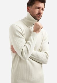 Gebreide crèmekleurige pullovertrui met een hoge kraag, geribbelde textuur, lange mouwen en een getailleerde silhouet, met een subtiel logo op de mouw.