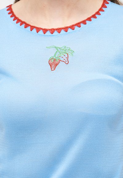 Μπλε πλεκτό τοπ με κόκκινο τρίγωνο περιθώριο στη λαιμόκοψη και μικρές κεντημένες κόκκινες φράουλες με πράσινα φύλλα στο στήθος.