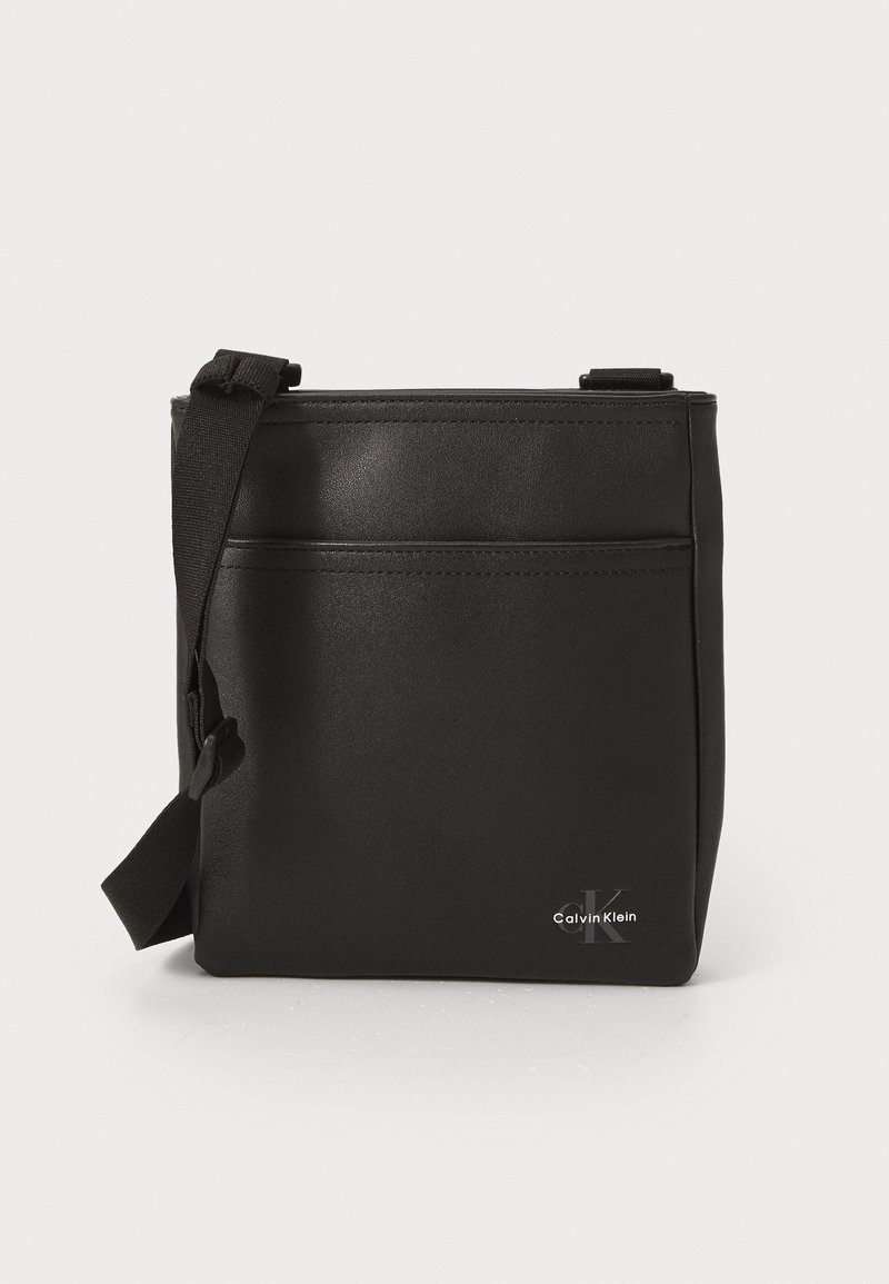 Borsa a tracolla nera in materiale sintetico di forma rettangolare, con tasca zippata frontale e logo Calvin Klein in argento nella parte inferiore.