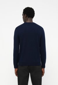 Navy blue knit sweater with long sleeves and a crew neck, featuring a smooth texture and ribbed hem. Worn over black pants.