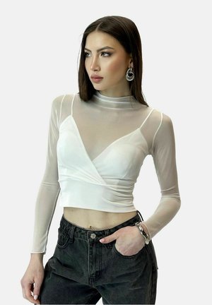 Hvid langærmet top med gennemsigtigt stofoverlæg, har en indpakningsdesign og tætsiddende bodice. Bæres med højtaljede sorte bukser.