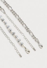 Collier en chaîne argentée à trois couches, comportant des perles rondes en argent et en perles, avec des maillons de formes variées et une fermeture à clip en forme de homard.