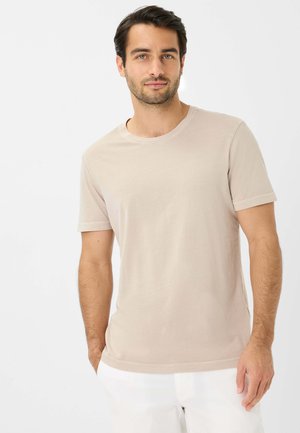 Beige kortærmet T-shirt i bomuldsblanding, med rund halsudskæring og subtile syninger, båret af en person med mørkt hår.