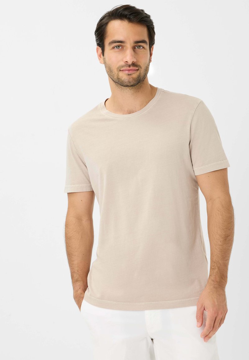 Beige kortærmet T-shirt i bomuldsblanding, med rund halsudskæring og subtile syninger, båret af en person med mørkt hår.