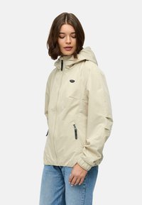 Beżowa, lekka kurtka z kapturem, z przodu na zamek błyskawiczny i dwoma bocznymi kieszeniami. Elastyczne mankiety i dół zapewniają wygodne dopasowanie.