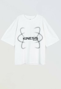 Biała, oversize koszulka z czarnymi abstrakcyjnymi wzorami w kształcie spirali otaczającymi słowo "KINESIS" oraz mniejszym tekstem "podświadomość" poniżej.
