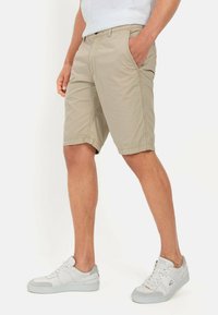 Beige katoenen shorts met een klassieke snit, voorzien van pockets en subtiele stikdetails, gecombineerd met witte sportieve sneakers.