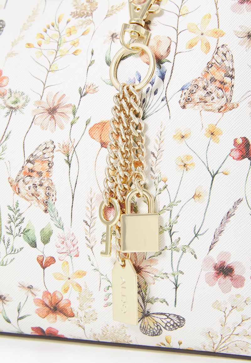 Sac à main à motif floral avec un fond blanc texturé, matériel doré, accents en chaîne et détails décoratifs en forme de clé et de cadenas.