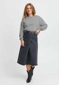 Faldita de mezclilla en gris oscuro con cintura alta, completada con un cierre de botón y detalles de costura. Combinada con una sudadera gris y botas negras.