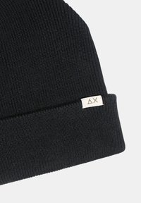 Berretto lavorato a maglia nero con texture a coste, dotato di risvolto e di un piccolo etichetta bianca con logo sul lato.