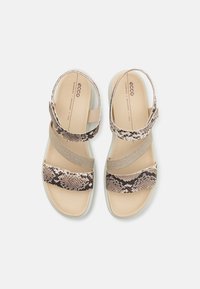 Ecco sandaalit, joissa on beige ja ruskea käärmeennahkakuosi. Niissä on kaksi leveää hihnaa ja tekstiilistä elastista nauhaa pehmeän pohjan päällä.