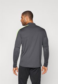 Heren poloshirt met lange mouwen in donkergrijze stof met neon groene schouderaccenten. Beschikt over een klassieke kraag en een getailleerd ontwerp voor sportieve kleding.
