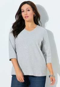 T-shirt grigia a manica tre quarti con scollo a V in tessuto morbido, vestibilità rilassata, con design semplice. Abbinata a denim blu scuro.