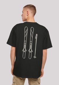 Black t-shirt with a white graphic design featuring two skis and a ski pole on the back. Short sleeves, relaxed fit, made of cotton.