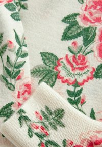 Blumiger Strickstoff mit roten Rosen und grünen Blättern auf einem cremigen Hintergrund, mit gerippten Details an den Bündchen und am Ausschnitt.