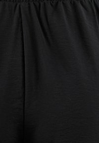 Zwarte stof met een gladde textuur en een lichte glans. Elastische tailleband boven een relaxte pasvorm, zonder zichtbare patronen of hardware.