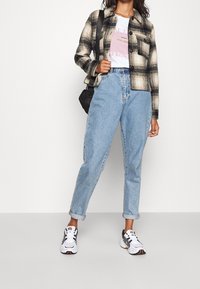 Czarna i biała kurtka w kratę na białym T-shircie z nadrukiem, zestawiona z jasnoniebieskimi dżinsami i czarno-białymi trampkami. Prosta czarna torebka na ramię.