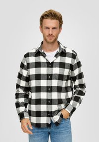 Zwart-wit geblokte flanellen shirt met knoopsluiting, lange mouwen en een zak. Gecombineerd met lichtblauwe spijkerbroek.