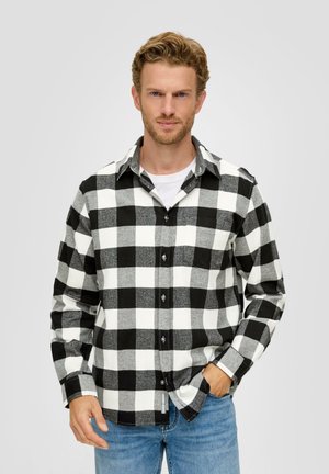 Schwarz-weiß karierte Flanellhemd mit Knopfverschluss, langen Ärmeln und einer Tasche. Kombiniert mit hellblauen Jeans.