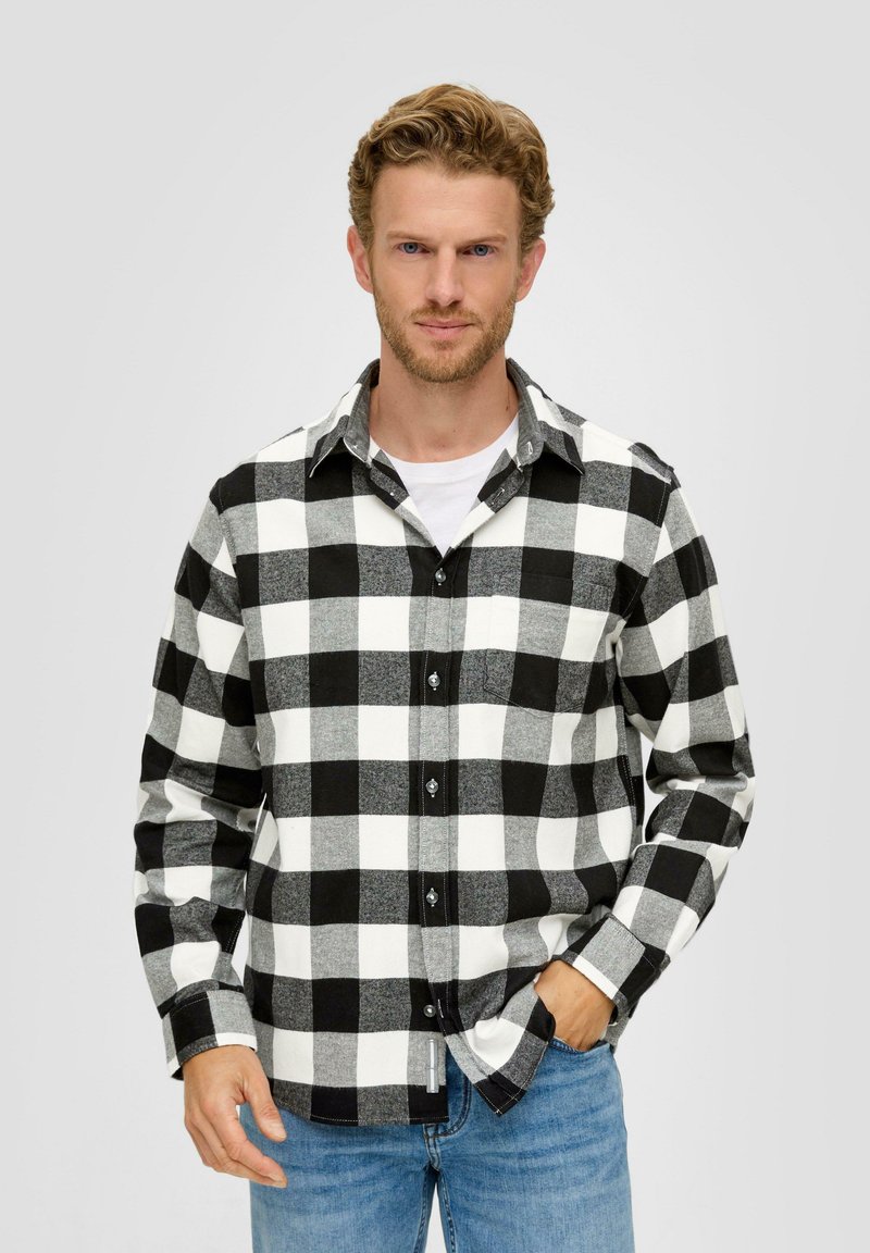 Zwart-wit geblokte flanellen shirt met knoopsluiting, lange mouwen en een zak. Gecombineerd met lichtblauwe spijkerbroek.
