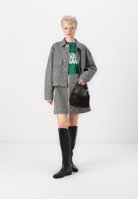 Chaqueta y falda de tela a rayas en gris, con una camiseta gráfica verde debajo. Botas negras hasta la rodilla y un pequeño bolso oscuro completan el look.