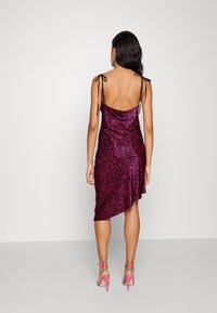 Fuksjowa sukienka satynowa z ciemnym abstrakcyjnym wzorem, asymetrycznym dołem oraz cienkimi regulowanymi ramiączkami, w zestawie z różowymi sandałami na obcasie.