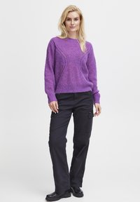 Pull en tricot violet avec un motif texturé et des coutures latérales, associé à un pantalon cargo noir. Le pull a une coupe décontractée et des manches longues.