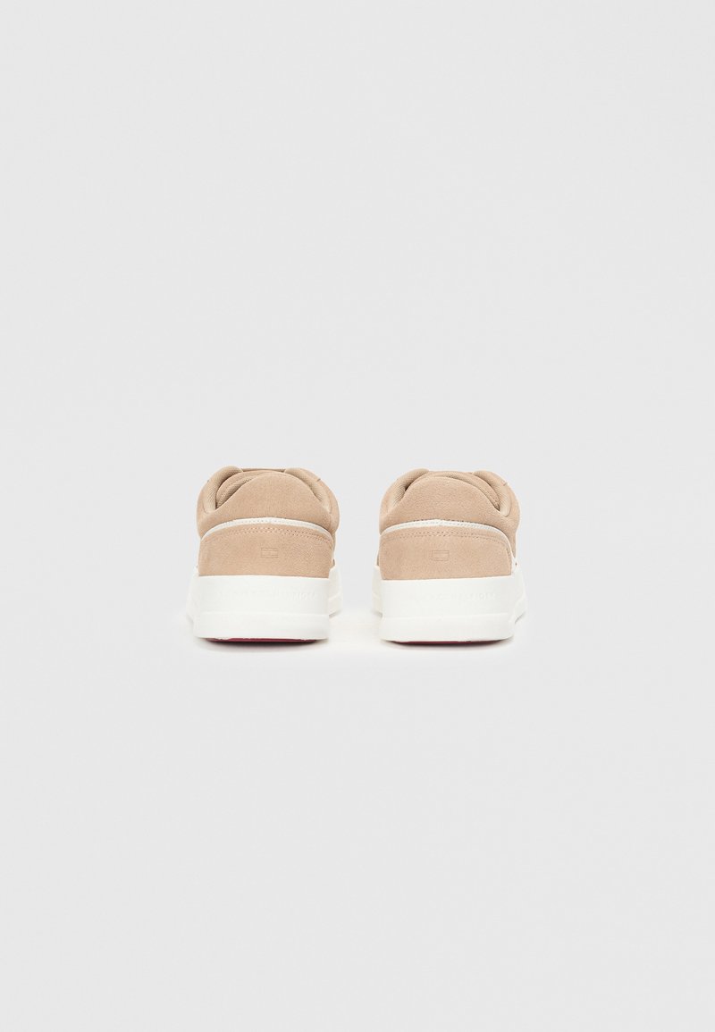 Baskets en daim beige avec une semelle en caoutchouc blanche. Talon arrondi, col rembourré et design minimaliste. Détails rouges au bas de la semelle.