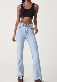 Jasnoniebieskie dżinsy z szerokimi nogawkami, wykonane z denimu, z wysokim stanem, posiadające kieszenie z przodu i zapięcie na guziki. W zestawieniu z czarnym crop topem.
