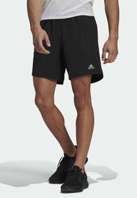 Zwarte sportshorts met een elastische tailleband en het grijze Adidas-logo aan de linkerbenedenkant. Lichtgewicht, gladde stof.