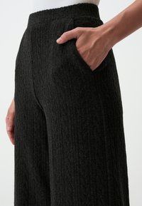 Pantaloni larghi a coste neri con un tessuto strutturato, dotati di vita alta elasticizzata e tasche laterali.