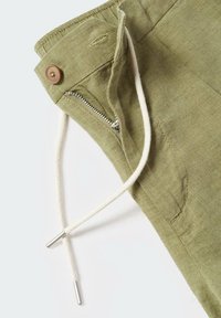 Pantalons en lin vert olive clair avec une poche zippée, une fermeture à bouton, et une taille à cordon avec des extrémités en métal argenté.