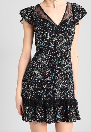 Czarna sukienka w kwiaty z koronkowym dekoltem w kształcie litery V i falbanianymi rękawami, ozdobiona drobnymi niebieskimi, różowymi i białymi kwiatami oraz falbanianym dołem.