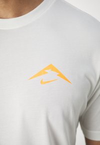 Camiseta de algodón blanca con un pequeño diseño gráfico naranja que presenta un rayo y el logo de Nike en el pecho. Mangas cortas, cuello redondo.