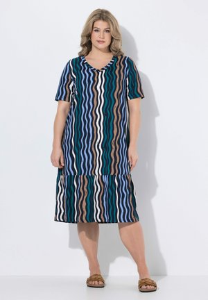 Femme portant une robe longueur genou à manches courtes avec des rayures verticales ondulées en bleu, vert, marron, blanc et noir.