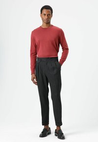 Rotes Langarmhemd kombiniert mit schwarzen Nadelstreifenhosen, die eine taillierte Passform und umgeschlagene Säume aufweisen. Schwarze Loafers vervollständigen das Outfit.