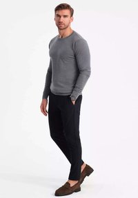 Graues Langarmshirt, kombiniert mit schwarzen Hosen, ergänzt durch braune Slipper. Glatter Stoff mit taillierter Passform und Rundhalsausschnitt.