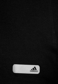 Tessuto di cotone nero con un'etichetta rettangolare bianca recante il logo adidas in nero, posizionata sulla superficie del capo.