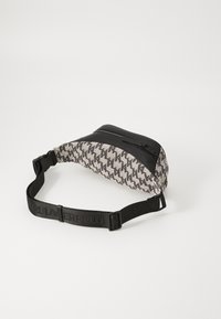 Fanny pack with a textured woven fabric in beige and dark brown zigzag pattern, featuring a black zippered top and adjustable strap.