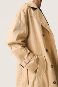Beige trenchcoat med dobbeltradet front, store brune knapper og en sidelomme. Har en bæltespænde på ærmekanten.
