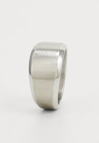 Silver ring with a smooth, polished finish and a slightly curved band. Engraved "GUESS" on one side. Simple, modern design.