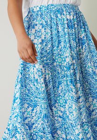 Blau gemusterter Rock mit einem gestuften Design; auf weißem Hintergrund mit kunstvollen Blumen- und abstrakten Formen, elastischer Taille.