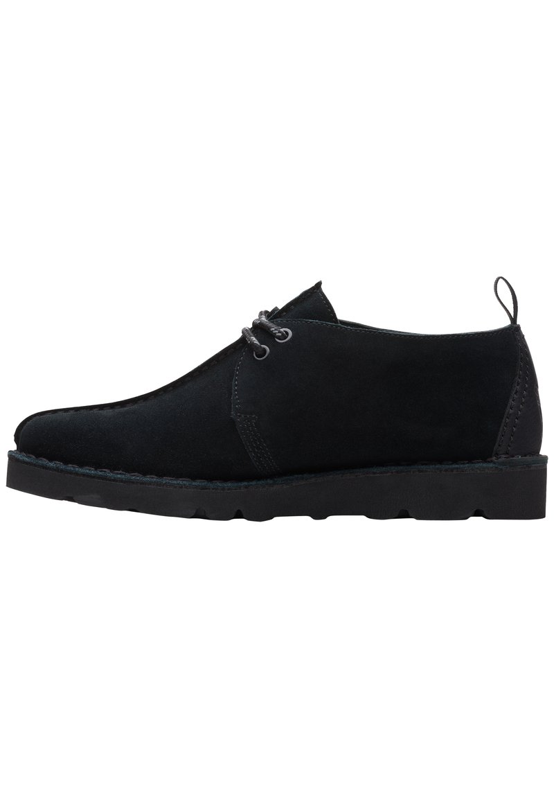 Schwarze Wildlederschuhe mit abgerundeter Zehenpartie, minimaler Schnürung und einer strukturierten Gummisohle. Niedriges Profil mit Nähten als Akzent.